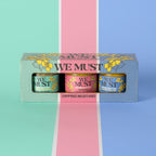 A brightly colored "We Must" Dipping Mustard box containing three 1.5 oz jars of Dipping Mustard. Cuvee Blanc Dipping Mustard, Fresh Dill Dipping Mustard, and Garden Yellow Dipping Mustard. 